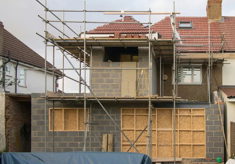 Semi-detached house under scaffolding, with a rooflight in its red-tiled roof and a new blockwork extension going up at the back