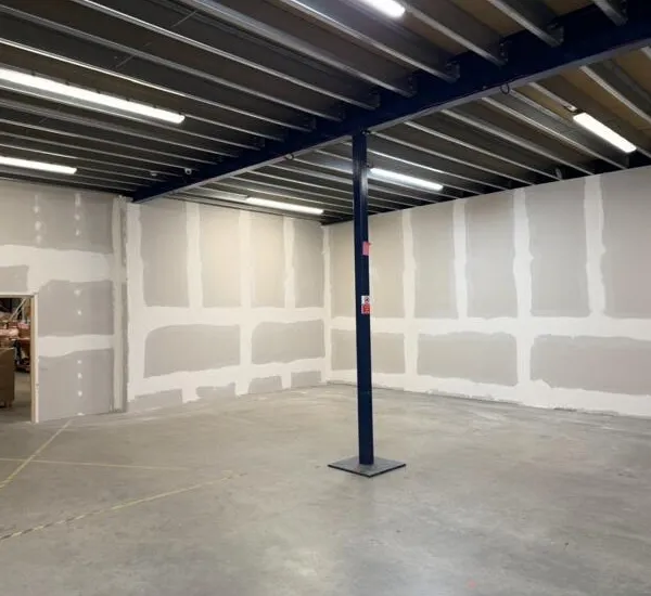 Finished space under the mezzanine, with taped and jointed plasterboard walls and a doorway through to the warehouse