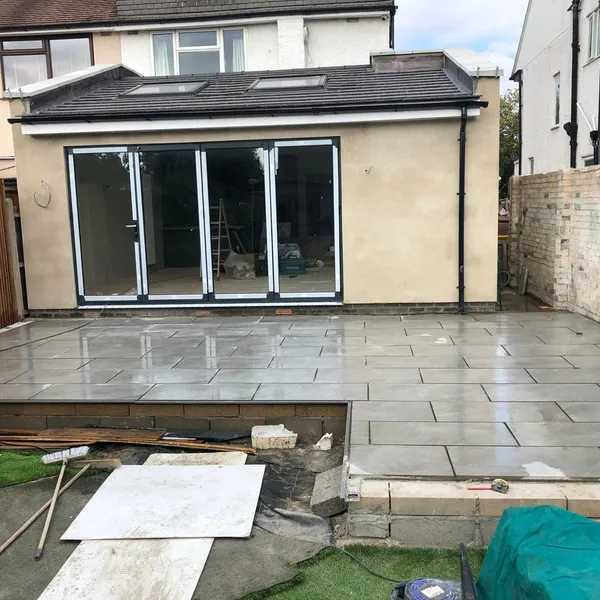Single-storey rear extension with a tiled roof, two rooflights and bifold doors, with the new paving being laid