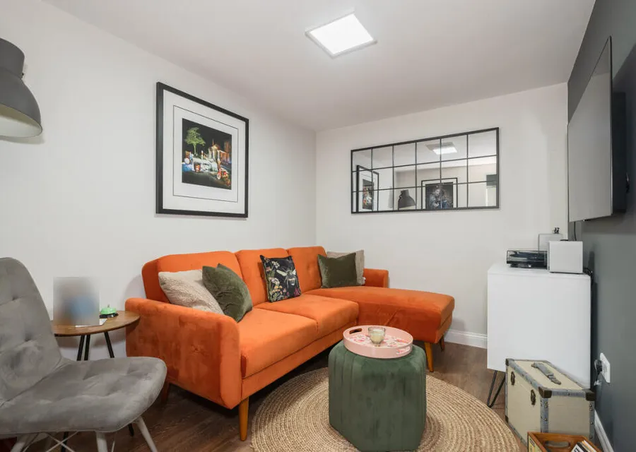 TV room in a garage we converted in Horsham, with an orange corner sofa, a wall-mounted television and a wood-effect floor