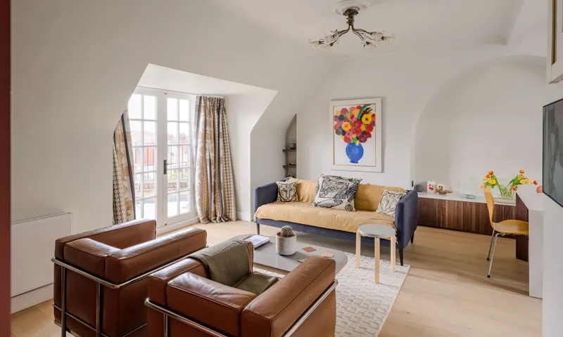 Living room of a top-floor flat we refitted, with leather armchairs, built-in shelving and French windows under the eaves