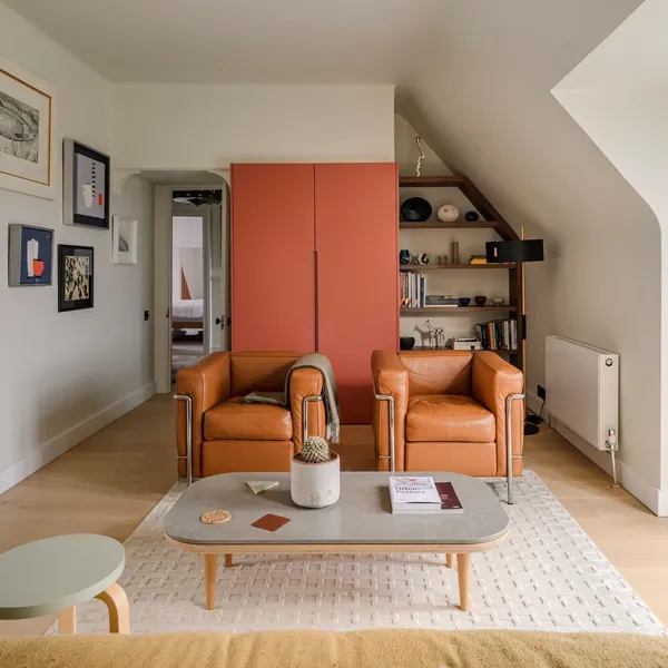 Living room with leather armchairs, a red built-in cupboard and shelving fitted into the slope of the eaves