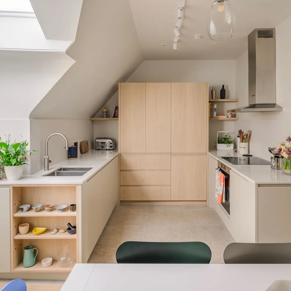 Pale oak kitchen fitted under a sloping loft ceiling, with a full-height tower of handleless units and a stainless steel extractor