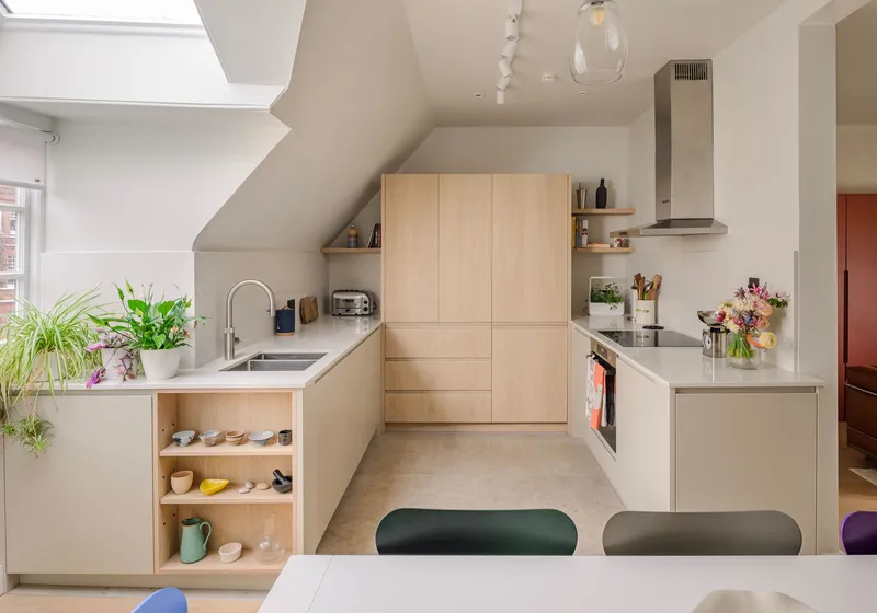 Pale oak kitchen fitted under a sloping loft ceiling, with a full-height tower of handleless units