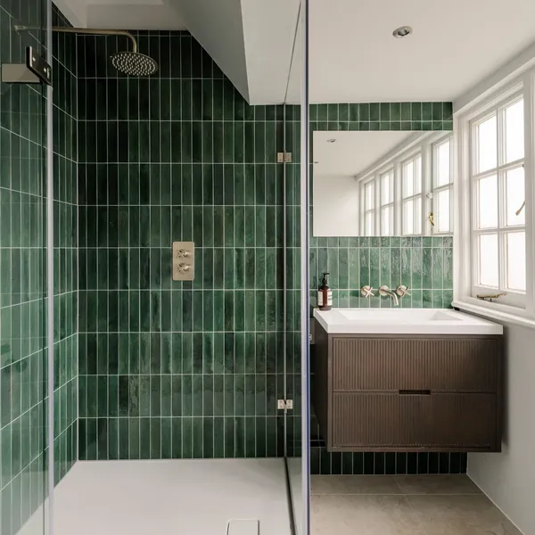 Shower room lined floor to ceiling in green glazed tiles, with a frameless glass screen and a dark wood vanity