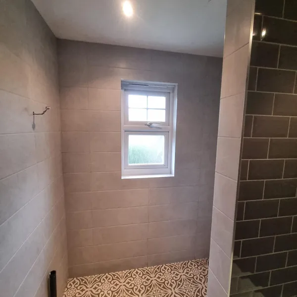 Shower room with large pale wall tiles, a window at the far end and a patterned tiled floor